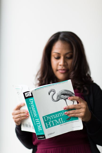 A woman with dark brown hair, dressed in a black blazer and maroon top, is holding and reading a gardening book titled 'Dynamic HTML' by O'Reilly. Her fingers are gently gripping the edges of the book